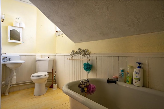 full bathroom featuring toilet, wood finished floors, vaulted ceiling, a freestanding bath, and wainscoting