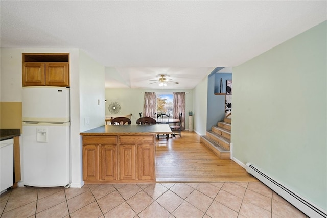 kitchen with light tile patterned floors, a peninsula, white appliances, and a baseboard radiator