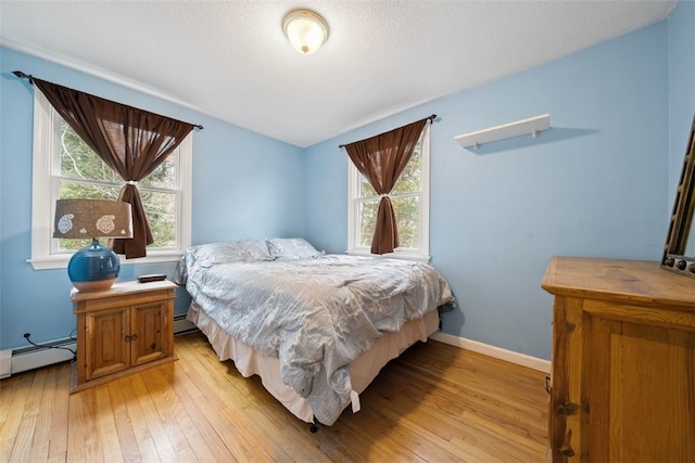 bedroom featuring a textured ceiling, light wood finished floors, baseboard heating, and baseboards