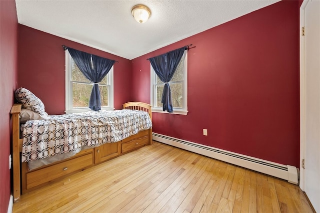 bedroom with a textured ceiling, baseboard heating, baseboards, and light wood-style floors