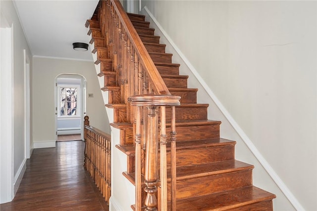 staircase with arched walkways, ornamental molding, wood finished floors, and baseboards