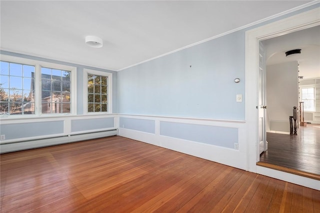 spare room with wainscoting, hardwood / wood-style flooring, ornamental molding, baseboard heating, and a decorative wall