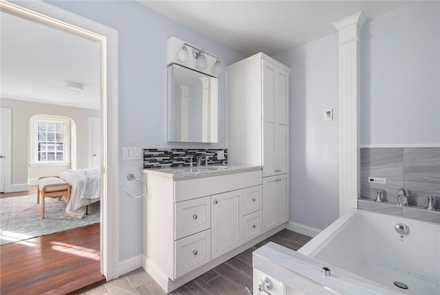 bathroom with backsplash, vanity, ensuite bath, wood finished floors, and a whirlpool tub