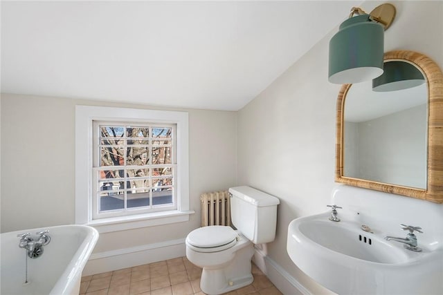 bathroom featuring radiator, toilet, a freestanding tub, baseboards, and tile patterned floors