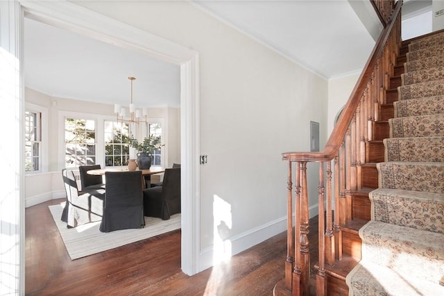 stairs with a notable chandelier, ornamental molding, wood finished floors, and baseboards