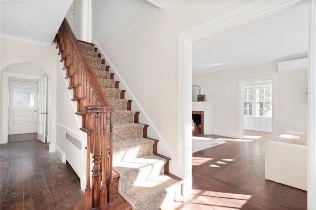 stairs featuring arched walkways, a fireplace, wood finished floors, an AC wall unit, and crown molding