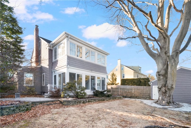 rear view of property with an outbuilding, fence, a sunroom, a storage unit, and a chimney