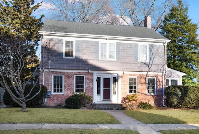 colonial home with a shingled roof, a front yard, brick siding, and a chimney