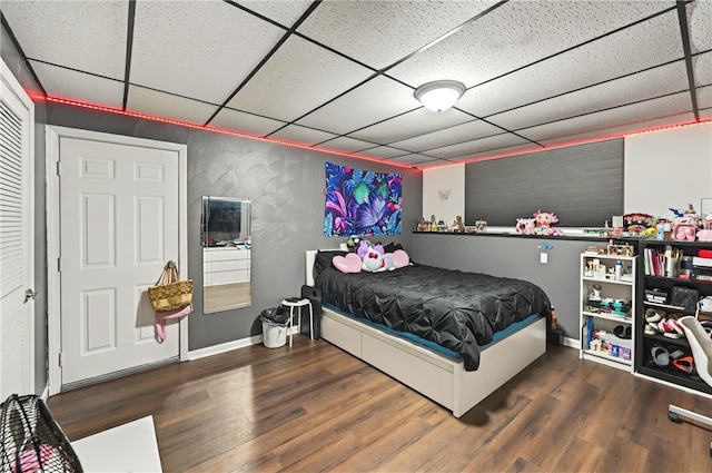 bedroom featuring a paneled ceiling, baseboards, and wood finished floors