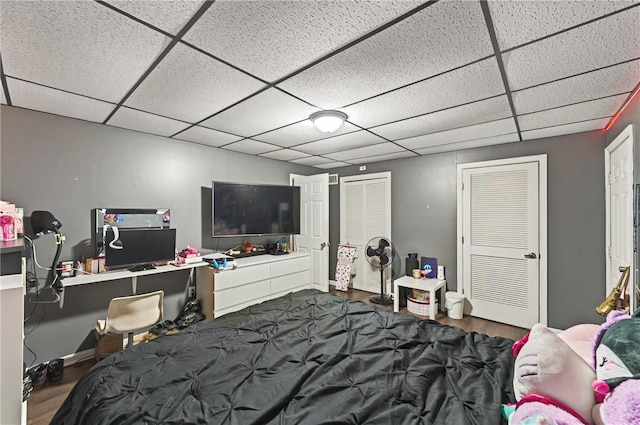 bedroom with a closet, a drop ceiling, wood finished floors, and baseboards