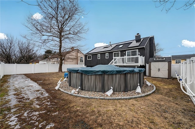 rear view of property with a fenced in pool, an outbuilding, solar panels, a storage unit, and a fenced backyard