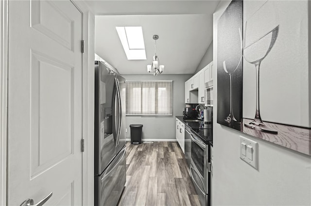 kitchen with stainless steel appliances, wood finished floors, a sink, baseboards, and white cabinets