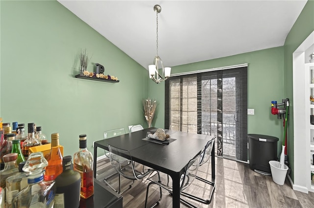 dining space featuring a chandelier, vaulted ceiling, wood finished floors, and baseboards