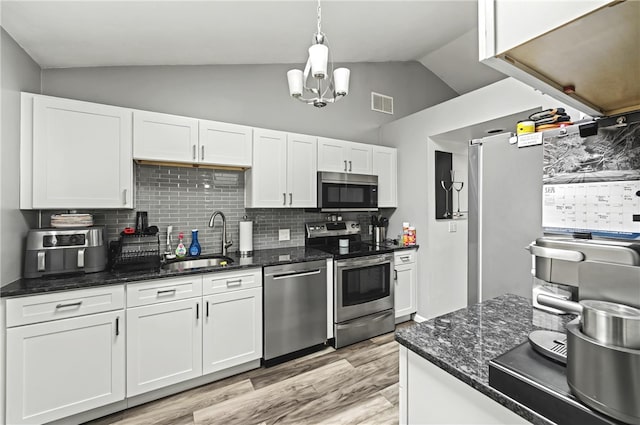 kitchen featuring visible vents, white cabinets, lofted ceiling, stainless steel appliances, and a sink