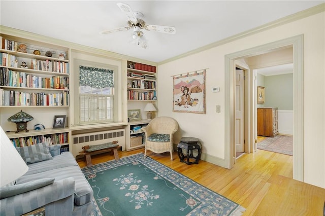 sitting room featuring built in shelves, wood finished floors, a ceiling fan, ornamental molding, and radiator heating unit