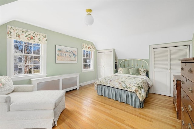 bedroom with lofted ceiling, light wood-style flooring, multiple windows, and two closets