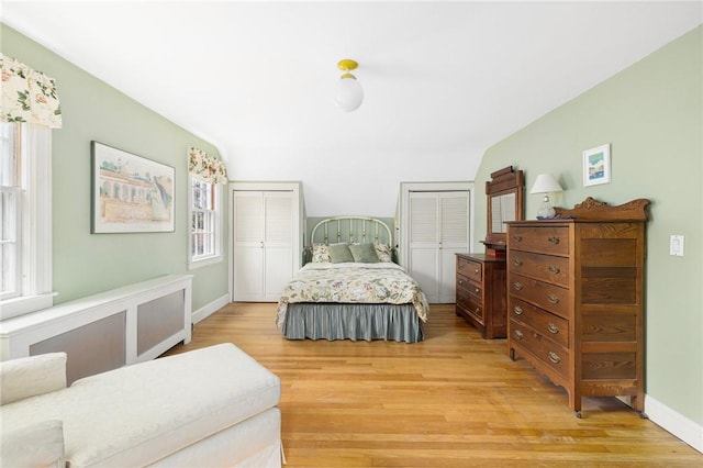 bedroom featuring baseboards, light wood finished floors, and two closets