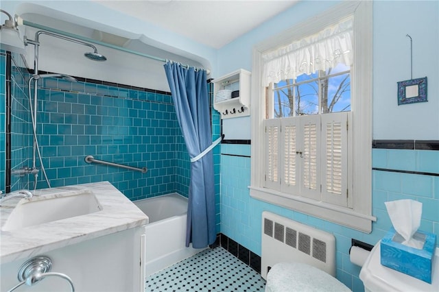 full bathroom with tile walls, toilet, radiator heating unit, shower / bath combo with shower curtain, and a sink