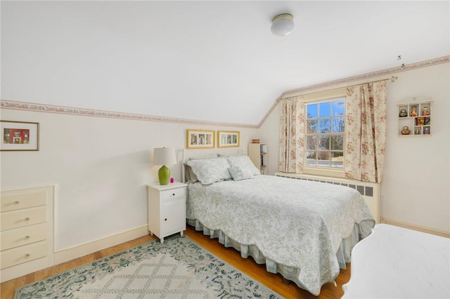 bedroom with lofted ceiling, radiator heating unit, baseboards, and light wood finished floors