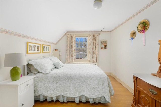 bedroom featuring lofted ceiling, light wood finished floors, baseboards, and ornamental molding