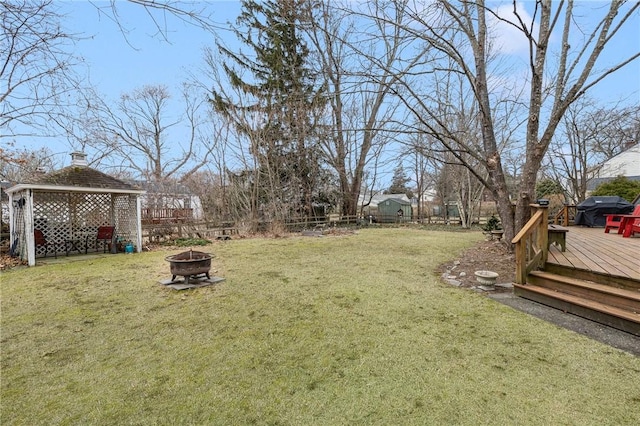 view of yard with a deck, fence, and a fire pit