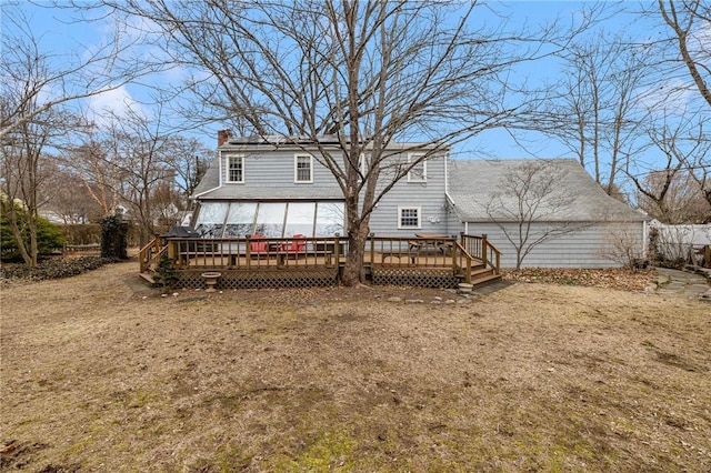 rear view of property featuring roof with shingles, a chimney, a wooden deck, and roof mounted solar panels