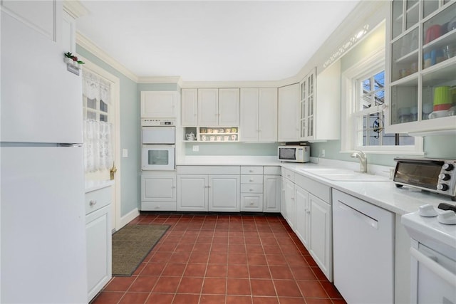 kitchen with white appliances, a sink, light countertops, ornamental molding, and glass insert cabinets