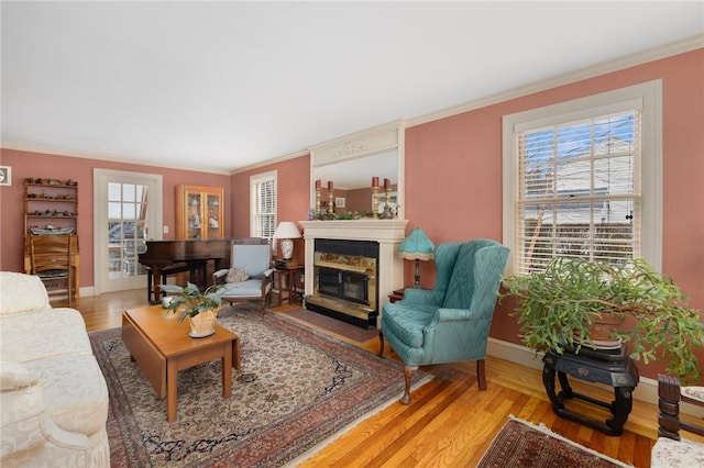 living room with crown molding, baseboards, wood finished floors, and a glass covered fireplace