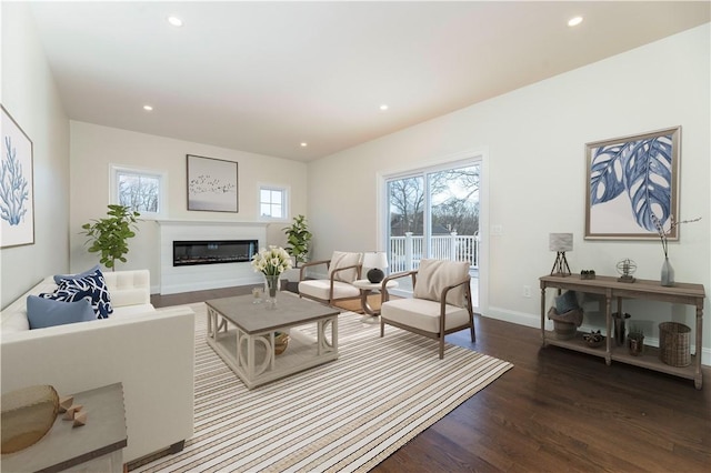 living room with dark wood-style flooring, a glass covered fireplace, a wealth of natural light, and recessed lighting