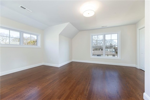 additional living space featuring dark wood-style floors, a wealth of natural light, visible vents, and vaulted ceiling