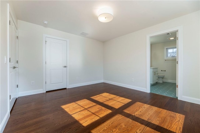 unfurnished bedroom featuring ensuite bath, baseboards, and wood finished floors