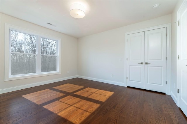 unfurnished bedroom with dark wood-style floors, a closet, visible vents, and baseboards