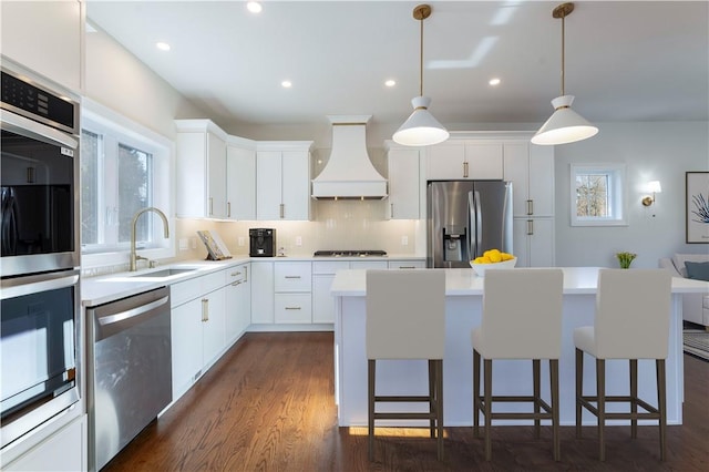 kitchen with a breakfast bar area, a center island, stainless steel appliances, premium range hood, and a sink