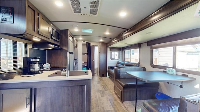 kitchen featuring light wood finished floors, light countertops, visible vents, open floor plan, and dark brown cabinetry