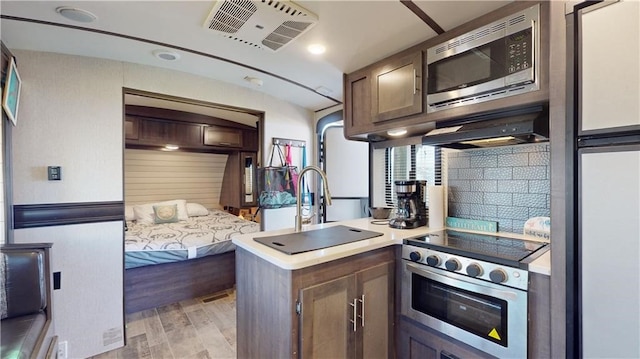 kitchen featuring visible vents, appliances with stainless steel finishes, a peninsula, under cabinet range hood, and backsplash