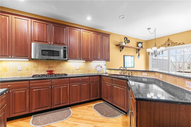 kitchen with appliances with stainless steel finishes, hanging light fixtures, a sink, light wood-type flooring, and backsplash