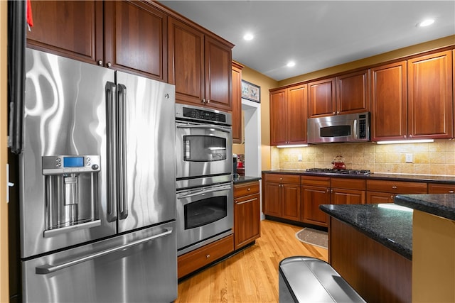 kitchen with dark stone counters, stainless steel appliances, light wood-type flooring, backsplash, and recessed lighting