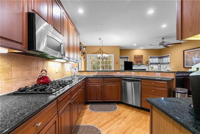 kitchen with stainless steel appliances, a peninsula, a sink, light wood-style floors, and decorative backsplash