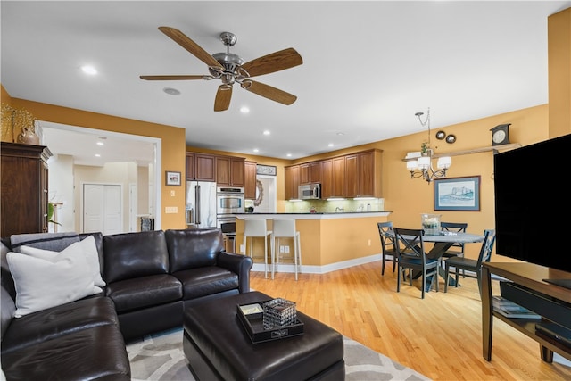 living area with ceiling fan with notable chandelier, light wood-type flooring, baseboards, and recessed lighting