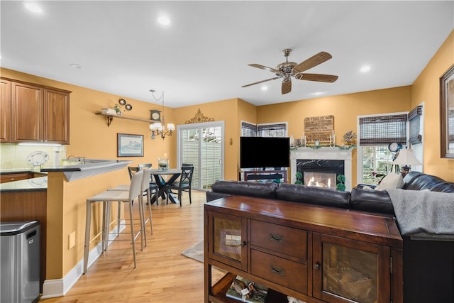 living room featuring recessed lighting, a fireplace, light wood finished floors, and ceiling fan with notable chandelier