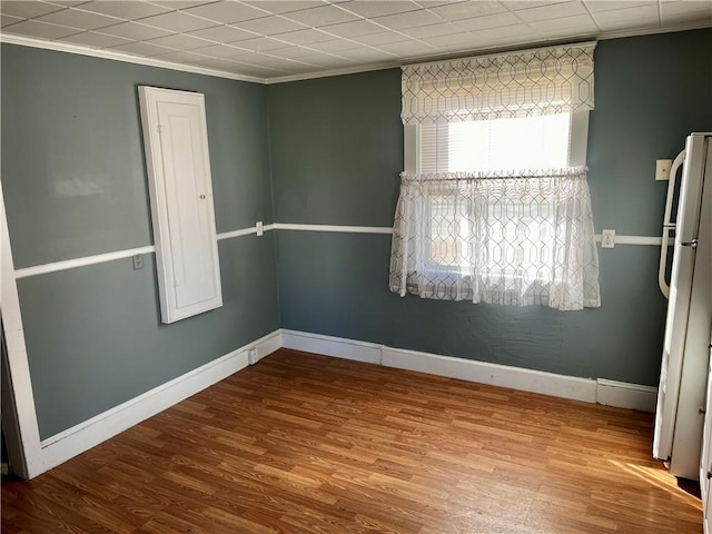 spare room featuring ornamental molding, baseboards, and wood finished floors