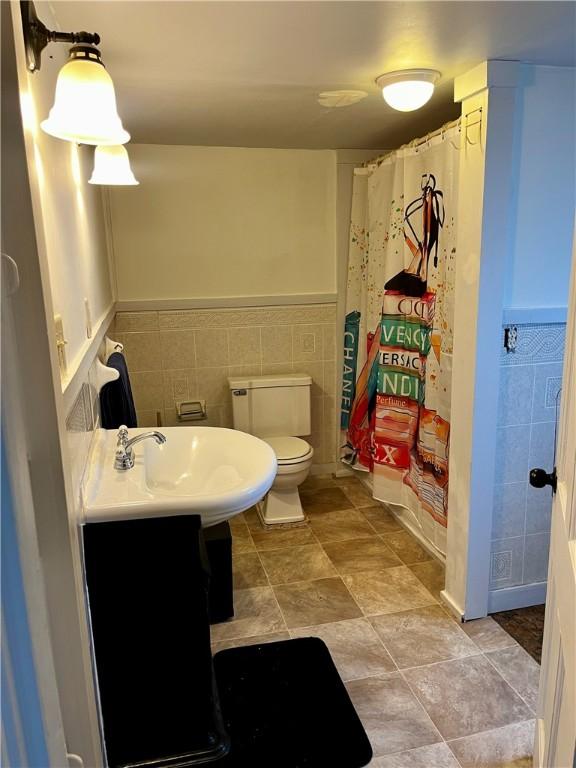 full bathroom with wainscoting, a shower with shower curtain, toilet, and tile walls