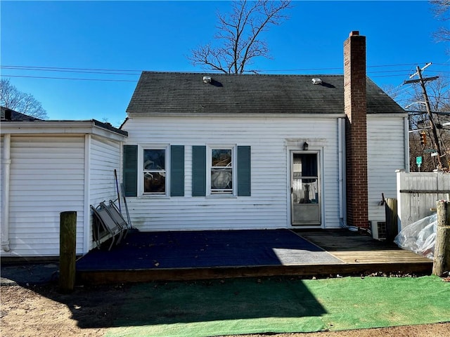 rear view of house featuring a shingled roof, a chimney, fence, and a deck