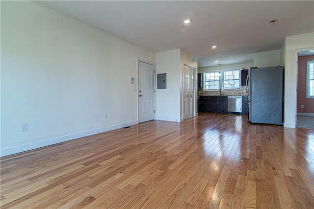 unfurnished living room with light wood finished floors, electric panel, baseboards, and a sink