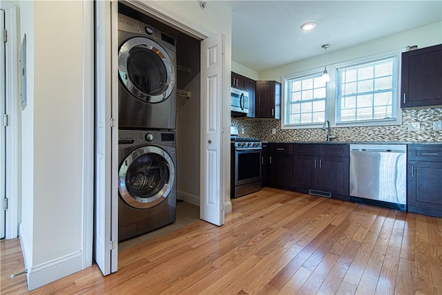 laundry room with stacked washer and clothes dryer, light wood finished floors, visible vents, a sink, and laundry area