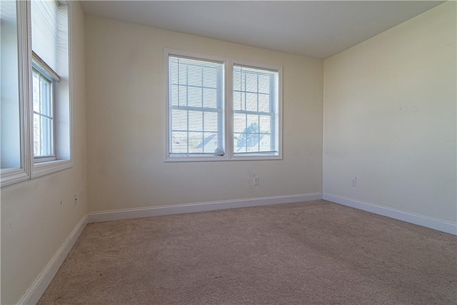 carpeted spare room featuring a healthy amount of sunlight and baseboards