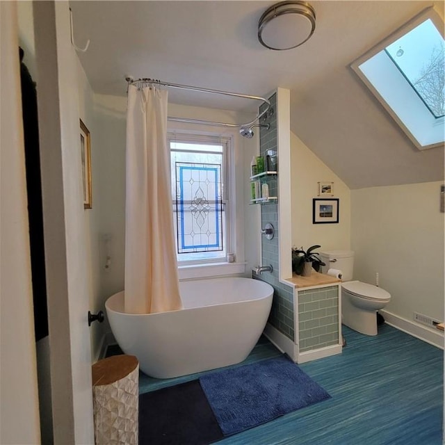 bathroom with toilet, wood finished floors, visible vents, baseboards, and lofted ceiling with skylight