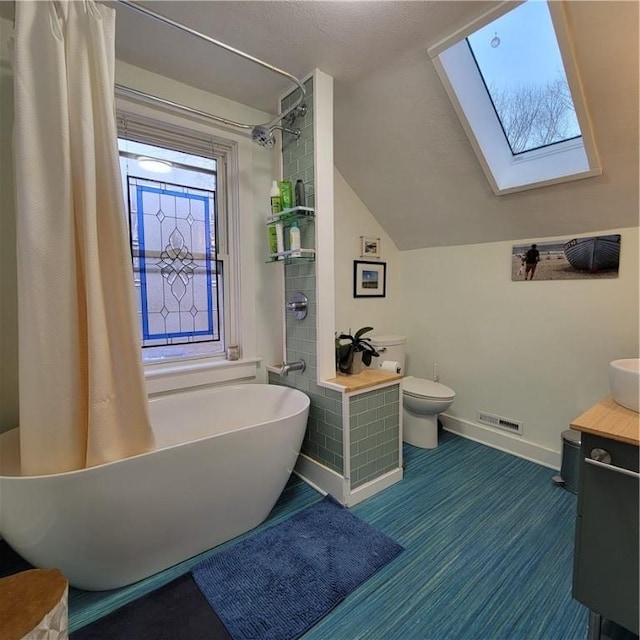 full bathroom featuring vaulted ceiling with skylight, toilet, vanity, a freestanding bath, and a shower with curtain