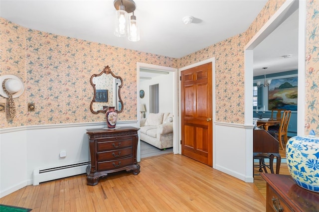 interior space featuring wallpapered walls, a baseboard radiator, a wainscoted wall, and wood finished floors