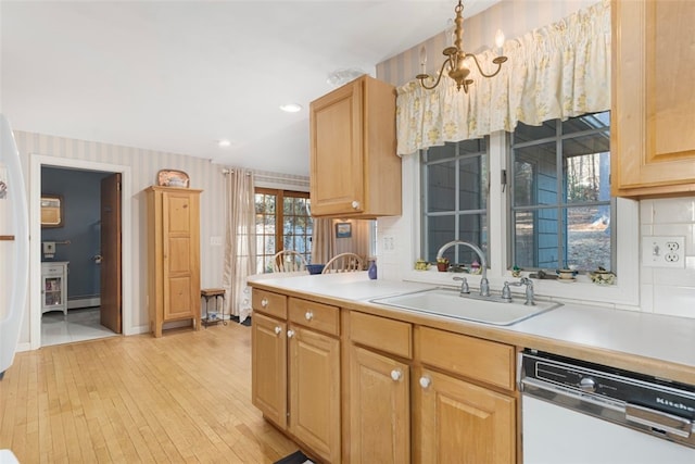 kitchen with white dishwasher, a sink, light countertops, baseboard heating, and light wood finished floors